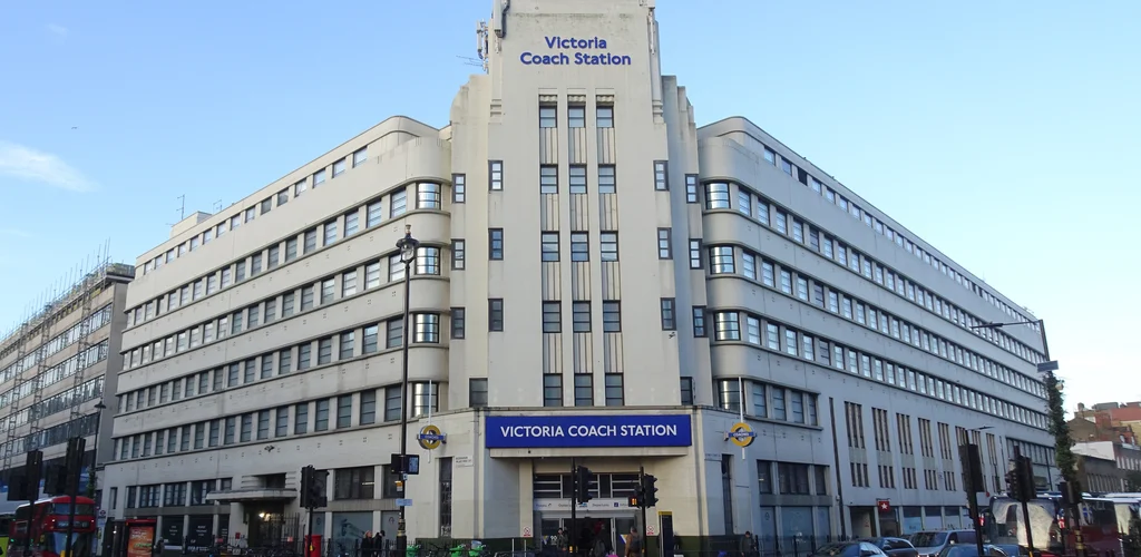 London Victoria Coach Station, a large Art Deco building with a busy street, featuring buses, cars, and pedestrians.